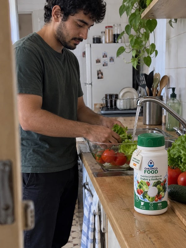 Hombre lavando lechuga y tomates en un barreño con el bote de Chilanco Food en la encimera